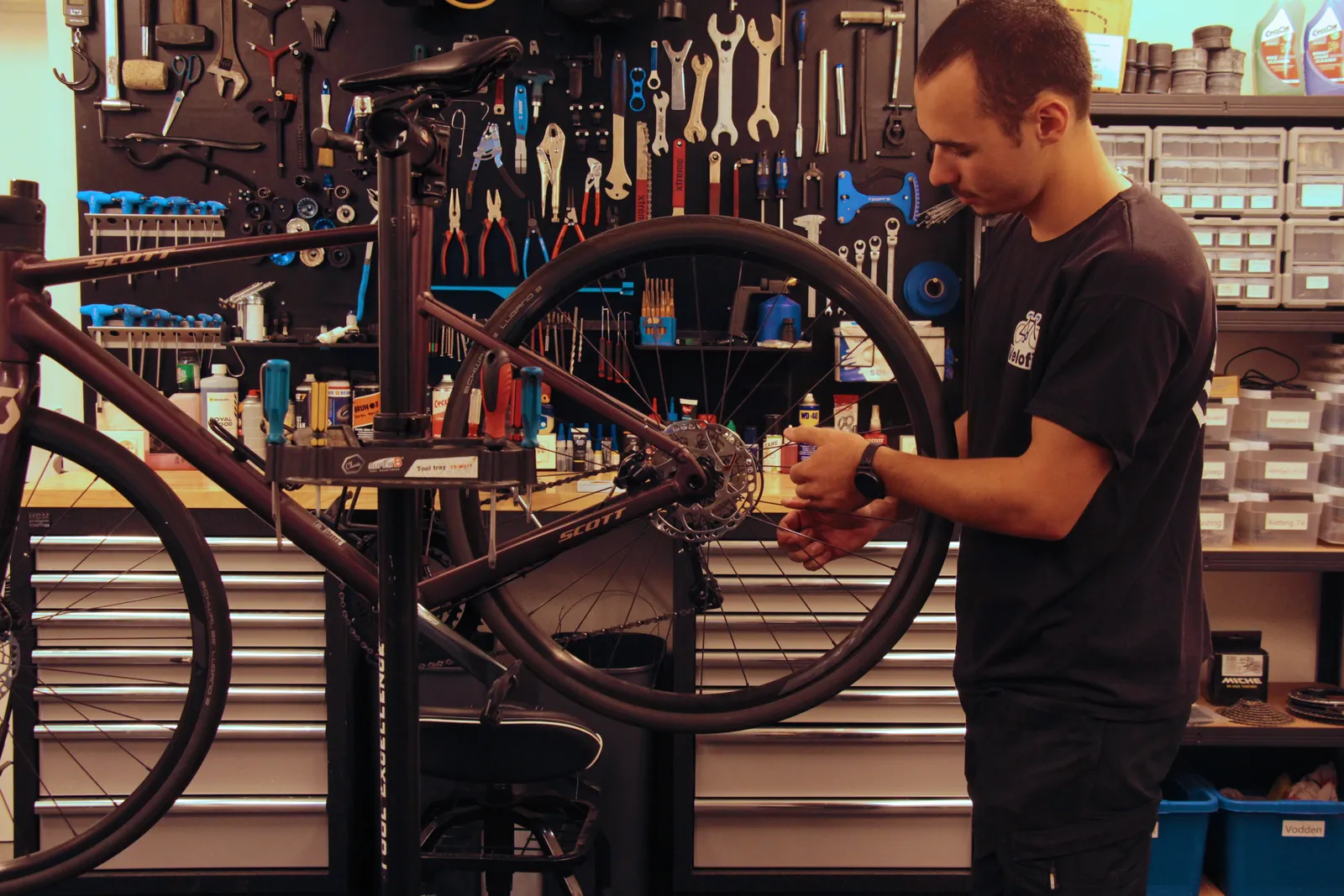 Mauro aan het werk aan een fiets in de werkplaats, met de gereedschapswand erachter
